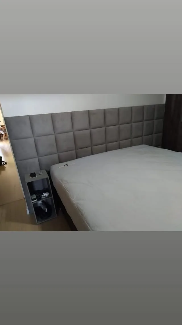 Cabeceira estofada em painéis de suede cinza cobrindo a parede do quarto